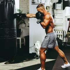 A muscular man punches a heavy bag in a gym, proving that boxing builds muscle.