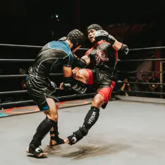 Two fighters in a ring, one delivering a powerful kick. The intensity of the moment showcases the mental fortitude and boxing psychology required for combat sports.