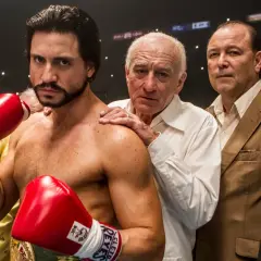 Roberto Duran, the legendary fighter, stands ready with red boxing gloves. His team, including Robert De Niro, offers support.