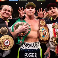 Canelo Alvarez, surrounded by his team, proudly displays multiple championship belts, a testament to his impressive boxing record.