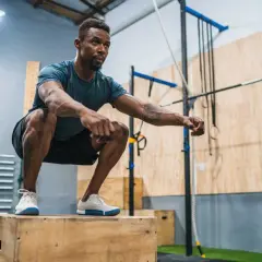 Man in squat position on a wooden box, preparing for explosive workouts.