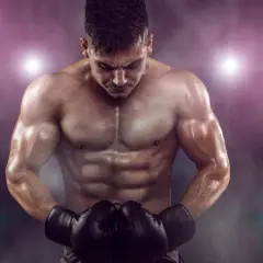 A muscular boxer with a defined boxer physique, wearing black gloves, looks down intensely under stadium lights.