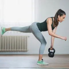 Woman performing kettlebell balance exercises, balancing on one leg while holding a kettlebell.