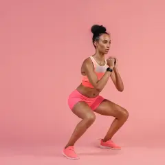 A woman in athletic wear performs pulsing squats, her hands clasped in front of her chest.