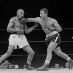 Two boxers in a ring, one landing a punch. The boxer on the right, with a powerful Rocky Marciano physique, is throwing a jab.