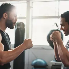 Two men in a gym, focused on their weight training for boxers. Punching bags and gym equipment are visible in the background.