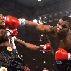 Mike Tyson prime lands a powerful punch in a boxing match, his opponent recoiling from the impact.
