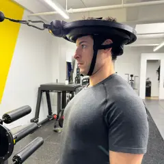 Man performing neck curls with a weighted harness in a gym.