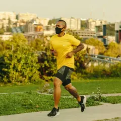 Man running with oxygen mask on a path, city skyline in background.