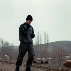 A boxer in a black tracksuit and beanie runs outdoors, training in the cold. This is why boxers run in hoodies: to sweat more and increase endurance.