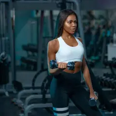 A woman with muscular arms lifts dumbbells in a gym, showcasing her dedication to fitness.