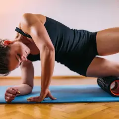 Woman performing a full body foam rolling routine on a blue mat, targeting her quadriceps.