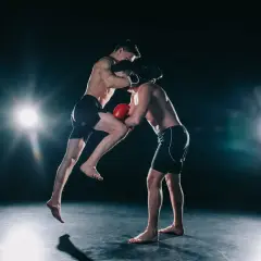 Two boxers spar intensely. One leaps, delivering a knee strike while the other defends. This dynamic action shows how boxers do calisthenics for explosive power.