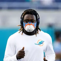 Miami Dolphins player running with an altitude mask training, headphones on, and giving a thumbs up.