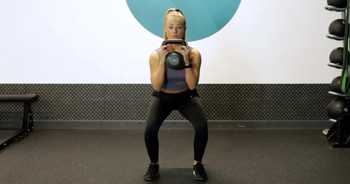 Woman performing kettlebell squat pulses in a gym.