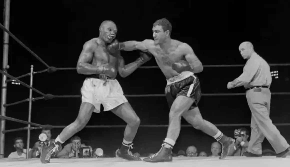 Two boxers in a ring, one landing a punch. The boxer on the right, with a powerful Rocky Marciano physique, is throwing a jab.