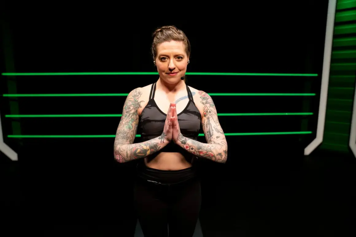 A tattooed woman in athletic wear holds her hands in prayer pose, ready for yoga for boxers.