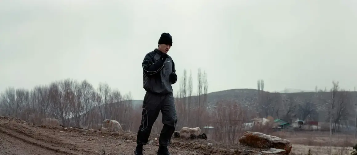 A boxer in a black tracksuit and beanie runs outdoors, training in the cold. This is why boxers run in hoodies: to sweat more and increase endurance.