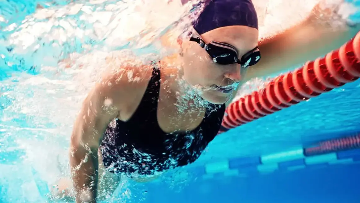 A swimmer in goggles and cap powers through the water. This image shows that boxers can swim, and do so with impressive strength and technique.