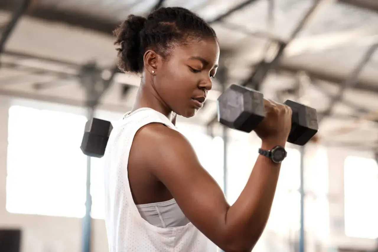 Focused woman performing bicep curls with a dumbbell, her forearm muscles engaged in a powerful punch-like motion.