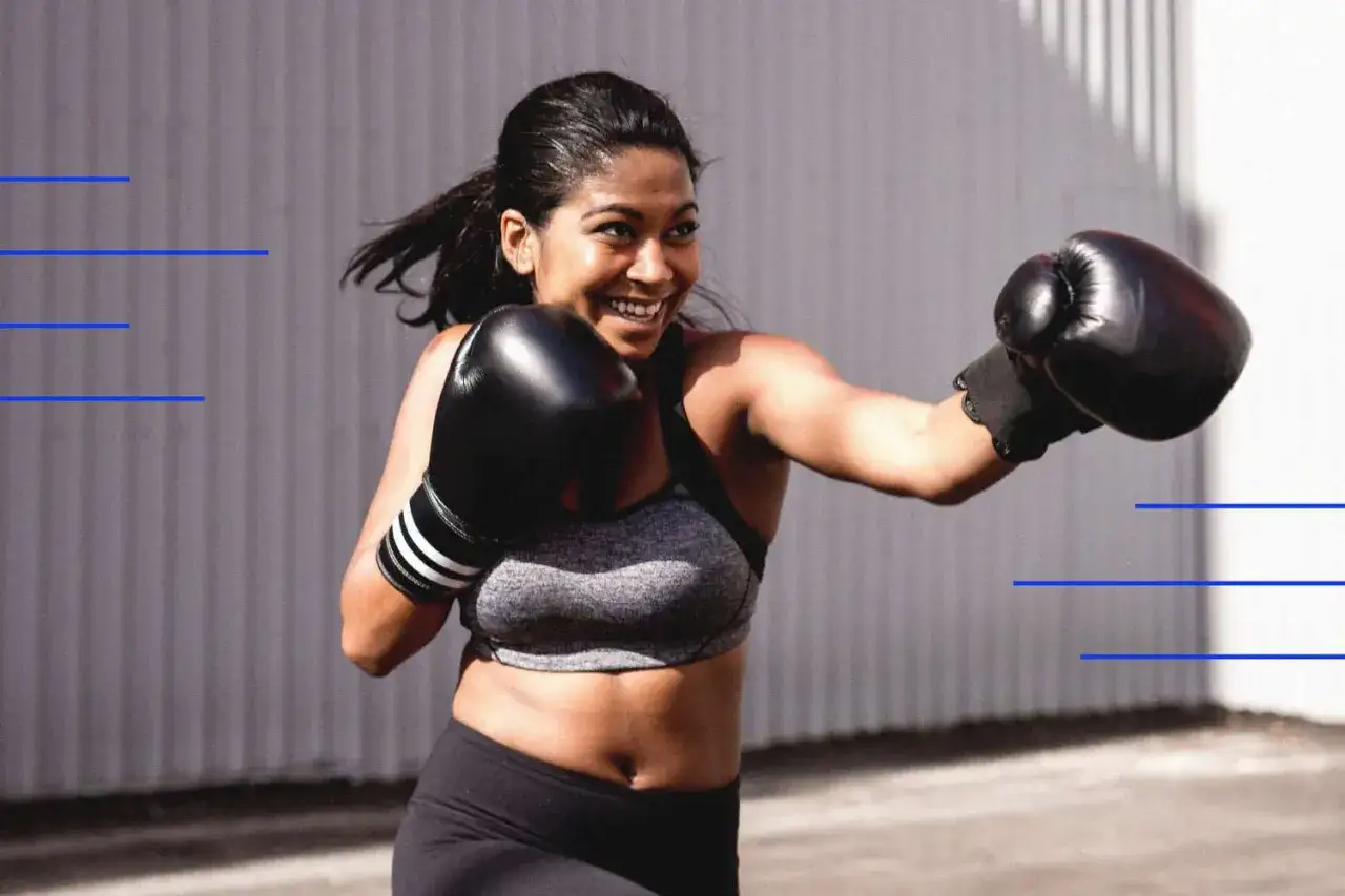 Woman in boxing gloves smiles while doing boxing weight training outdoors.