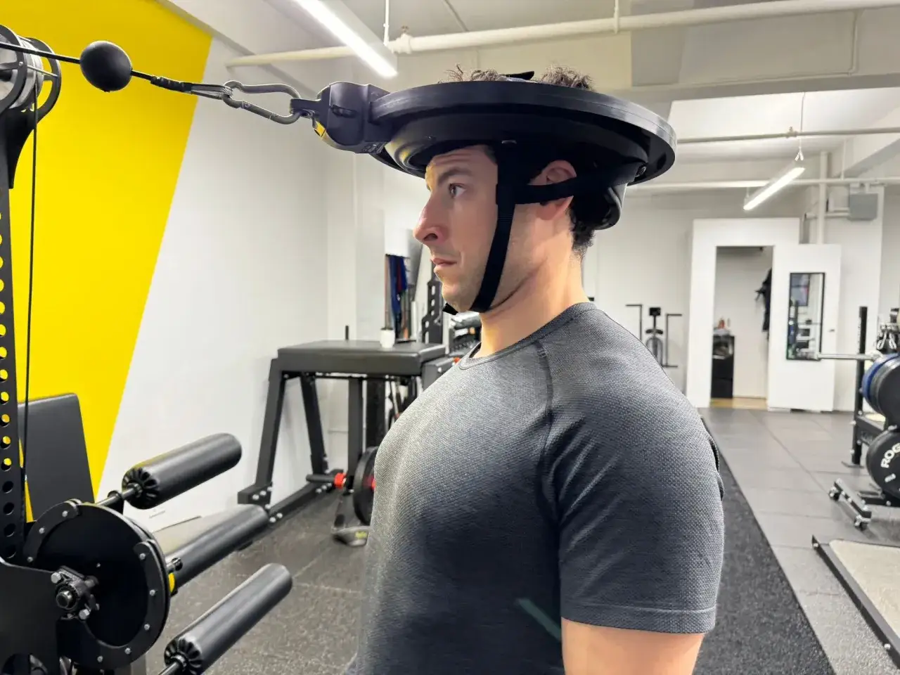 Man performing neck curls with a weighted harness attached to a cable machine in a gym.