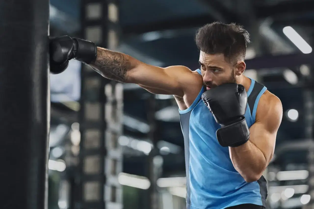 A boxer throws a punch, his tattooed arm extended. This intense workout is great for boxing calories burned.