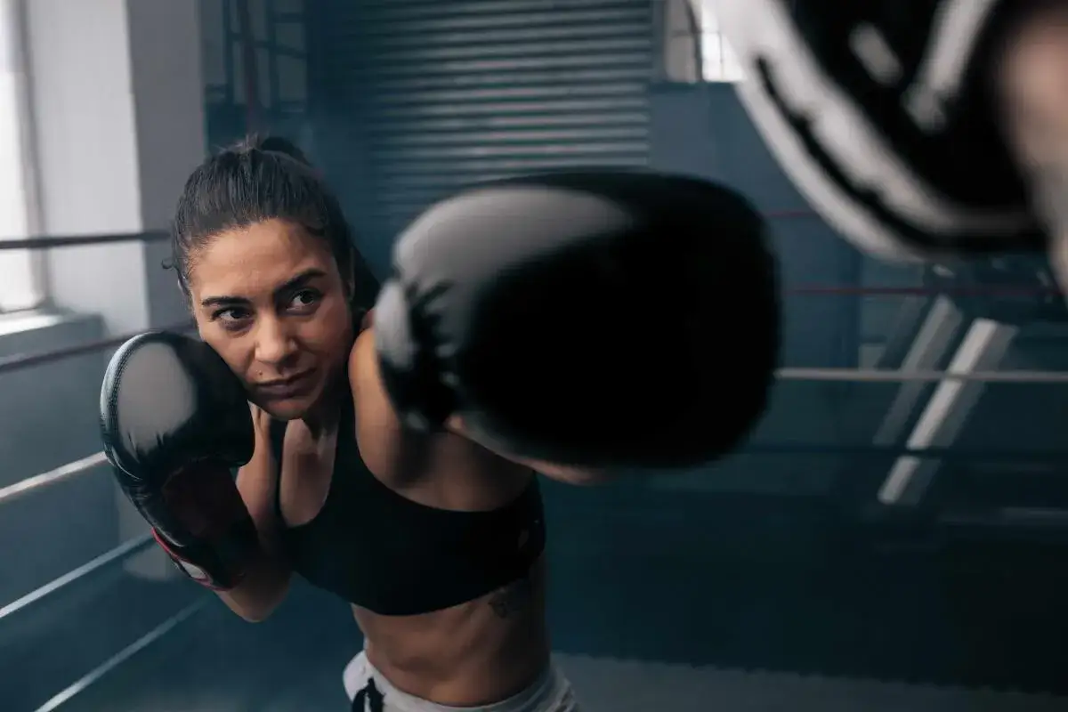 Focused woman in boxing gloves throws a punch during intense women boxing exercises in a ring.
