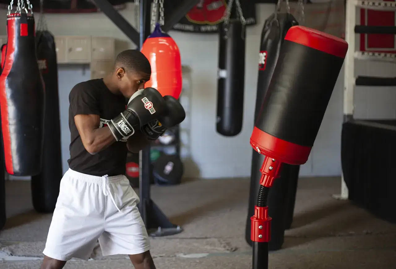 A man in boxing gloves trains, proving that boxing is good cardio. He's surrounded by various punching bags in a gym.