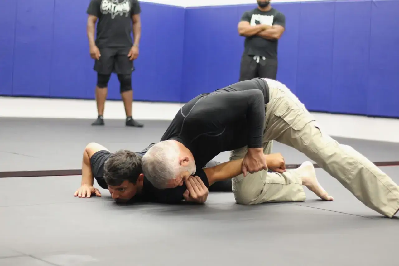 Two men grapple on a mat. One man, on his back, appears to be flinching a reflex as the other applies pressure.