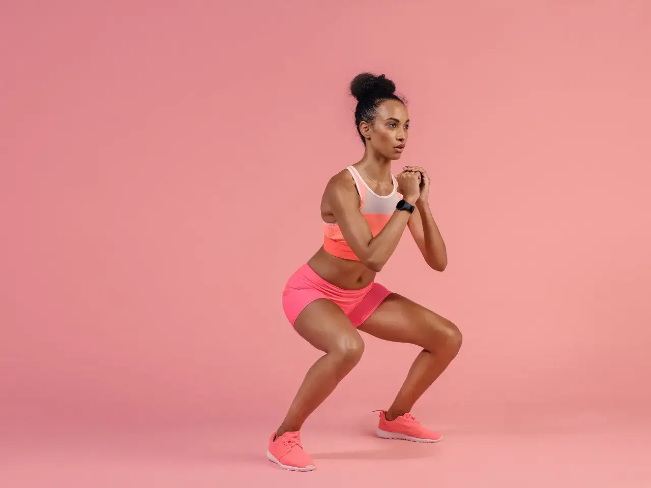 Woman performing squat pulses in pink athletic wear.