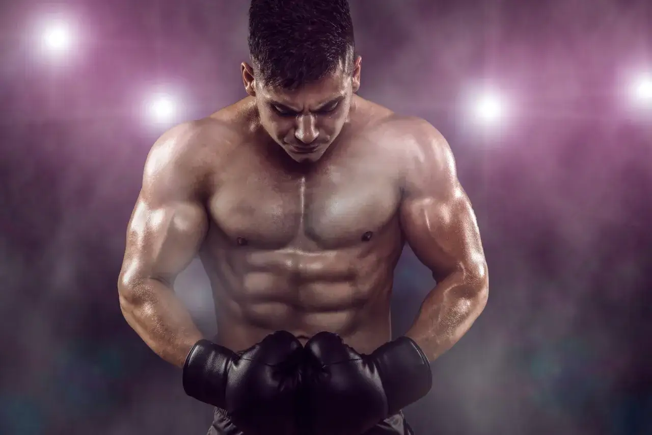 A muscular boxer with a defined boxer physique, wearing black gloves, looks down intensely under stadium lights.