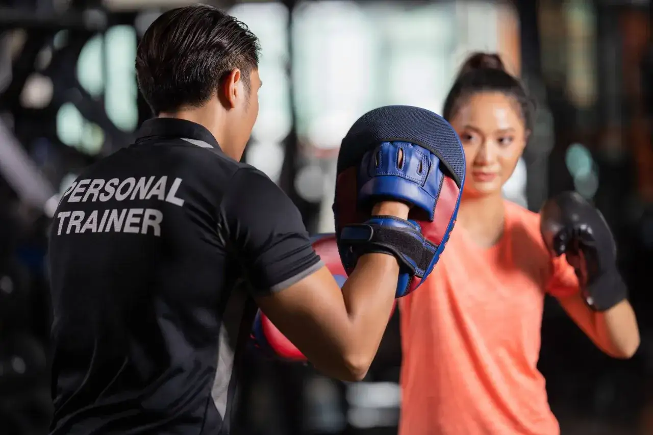 A personal trainer guides a woman in developing her boxing mindset, holding pads for her practice.