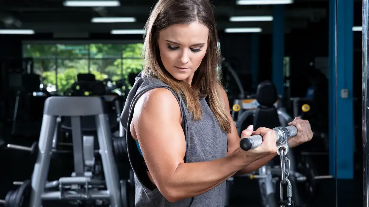 A woman with impressively muscular arms works out at the gym, focusing on her bicep curl.